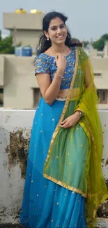 Woman in vibrant blue and green traditional attire on rooftop.