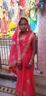 Woman in vibrant red traditional attire standing in front of cultural backdrop.