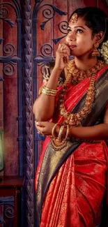 Elegant woman in traditional red saree and gold jewelry standing gracefully.