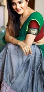 A woman elegantly dressed in a green traditional Indian saree sitting gracefully.