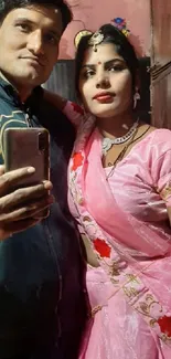 Traditional couple in pink attire taking a selfie.