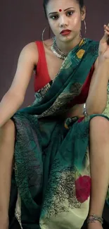 Woman in emerald green sari with jewelry, seated elegantly.