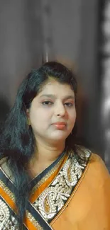 Portrait of a woman in a golden and orange sari against a blurred background.