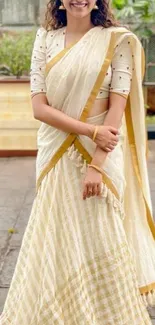 Elegant woman in cream and gold saree smiling outdoors.