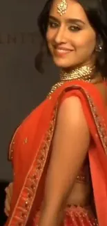 Woman wearing a vibrant red saree with intricate jewelry, exuding elegance.