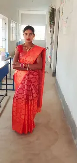 Woman in a red saree standing in a hallway.