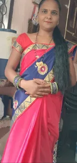 Woman in a red and gold saree posing gracefully indoors.