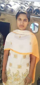 A young person in traditional attire outside a rustic home.