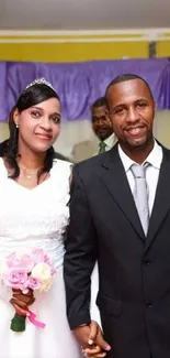 Happy couple in wedding attire with purple decor background.