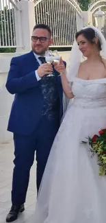 Elegant wedding couple holding glasses in a bright outdoor setting.