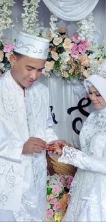 Wedding couple in white attire with floral decor background.