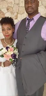 Wedding couple posing elegantly against stone wall.