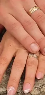 Intertwined hands with wedding rings on stone background.