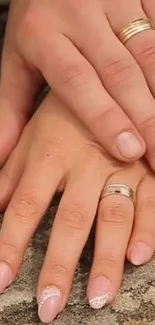 Intertwined hands with wedding rings on textured background.