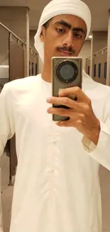 Man in white traditional attire taking mirror selfie.