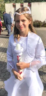 Girl in white dress holding candle at outdoor event.