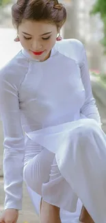 Woman in a traditional white dress sitting gracefully outdoors.