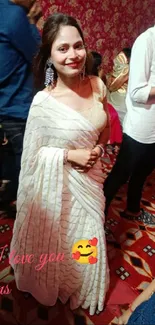 Woman in white saree at a vibrant event with red decor.