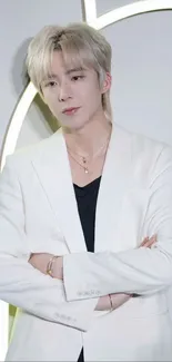 Portrait of a person in a white suit, arms crossed, against a minimalist background.