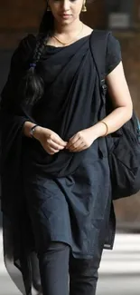 Woman in stylish black attire walking indoors.