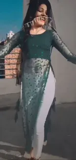 Woman in flowing teal dress dancing outdoors.