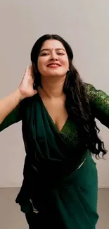 Woman in green sari poses elegantly against a plain background.