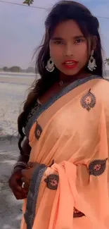 Elegantly dressed woman in a peach saree with a natural backdrop.