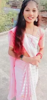 Woman wearing a pink saree stands outdoors, exuding elegance and style.