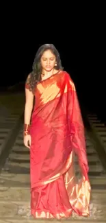 Woman in a red saree on railway track.