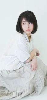 Elegant woman in white dress sitting on floor.