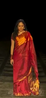 Woman in red sari walking on railway track at night.