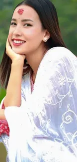 Elegant woman smiling in white floral attire with green background.