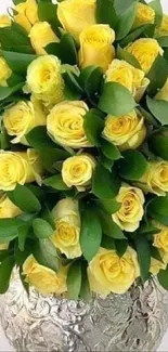 Yellow rose bouquet with green leaves in a silver vase.