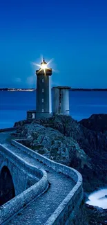 Coastal lighthouse at night with ocean and rocky path.