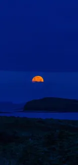 Full moon rising over dark blue night sky.