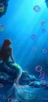 Mermaid sits on rock in vibrant blue ocean cave.