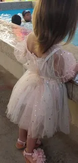 Child in sparkly pink dress by a poolside.