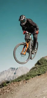 Mountain biker jumps against a turquoise sky with rugged landscape.