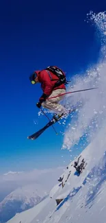 Skier in red jacket jumps off a snowy mountain with a deep blue sky backdrop.