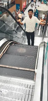 Man standing on an escalator in a bustling shopping mall.