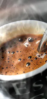 Espresso coffee in a black cup with a spoon on a reflective surface.