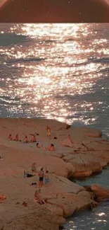 Sunset over a rocky beach with shimmering water reflections.