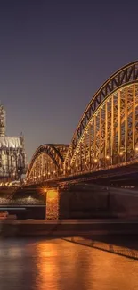 Night view of an illuminated bridge and cathedral reflecting on water.