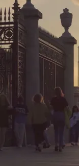 People walking by historic gates at sunset.