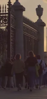 People walking near ornate gate at sunset.