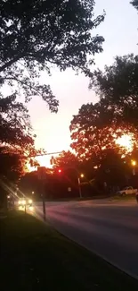 Urban road at sunset, silhouetted trees, and vibrant evening sky.