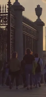 People walking past gates under a sunset sky.