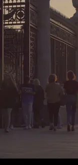 People walking past a decorative gate at sunset.