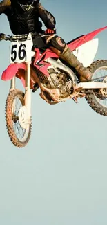 High-energy motocross bike jump against a clear blue sky, showcasing dynamic action.