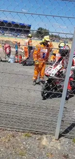 Motorcycle racer with team on track near fence, vibrant live-action scene.